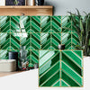 Emerald green herringbone marble peel-and-stick wall tiles installed on a wooden surface.