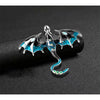 Silver enamel dragon brooch with iridescent blue and green accents on a black background
