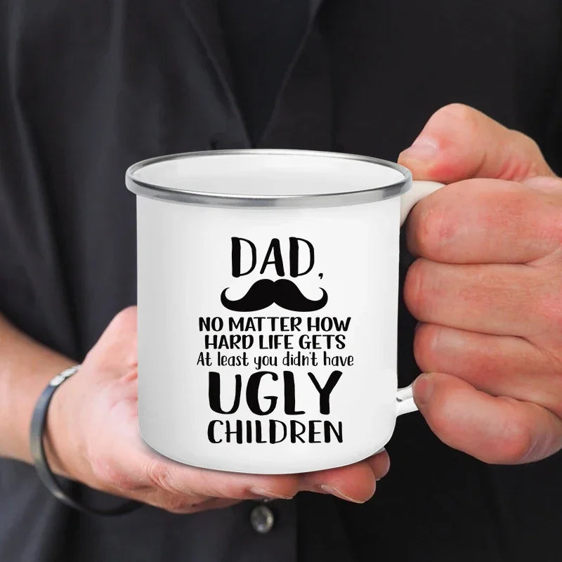 Une main tient une tasse à café en émail blanc avec l'inscription : Papa, peu importe la difficulté de la vie, au moins tu n'