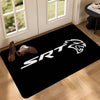 Black doormat featuring a white SRT logo and a pair of brown shoes on a wooden floor.