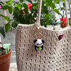 A handmade crochet keychain featuring a cute black and white panda charm attached to a beige woven bag.