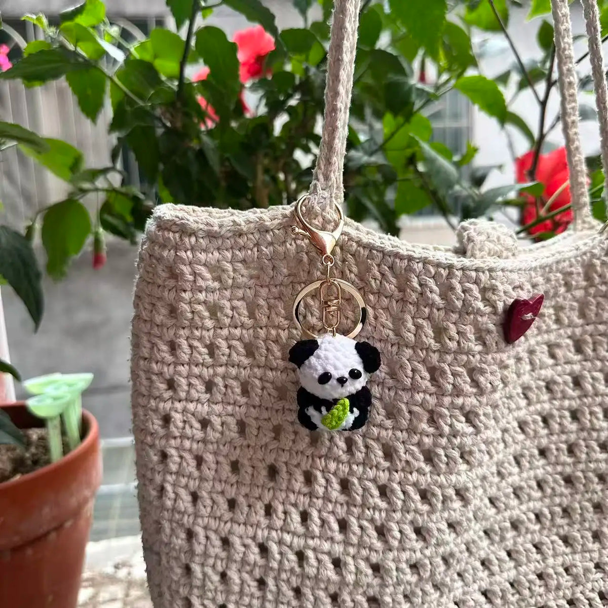 A handmade crochet keychain featuring a cute black and white panda charm attached to a beige woven bag.