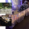 Elegant ice silk table skirt with matching top swag draped in white fabric and illuminated lights.