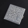 A silver stainless steel cigarette case with an embossed scroll pattern resting on a dark surface.