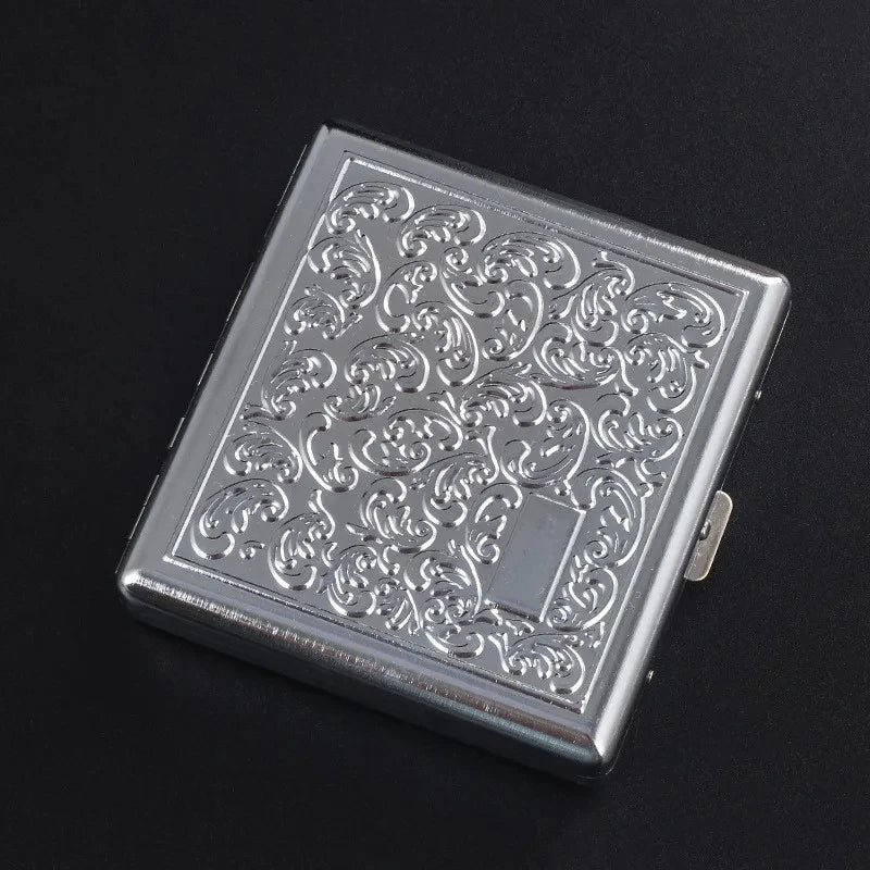 A silver stainless steel cigarette case with an embossed scroll pattern resting on a dark surface.