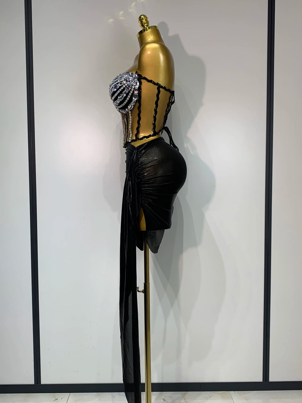 A black, sheer party outfit displayed on a gold mannequin featuring a beaded shoulder detail.