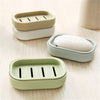 Three compact travel soap holders in beige and light green plastic are arranged on a wooden surface.