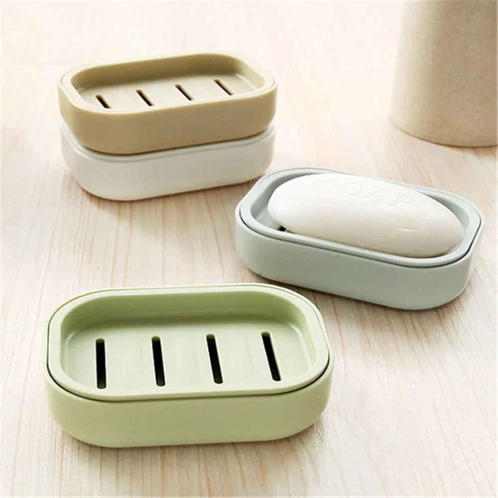 Three compact travel soap holders in beige and light green plastic are arranged on a wooden surface.