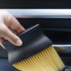 A hand is using a black car interior detailing brush set with soft yellow bristles on a car seat.
