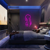 A neon sign shaped like a female silhouette is mounted on a dark wall above a modern bed.