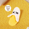 A yellow plush banana toy with a sad face is lying on a yellow textured surface.