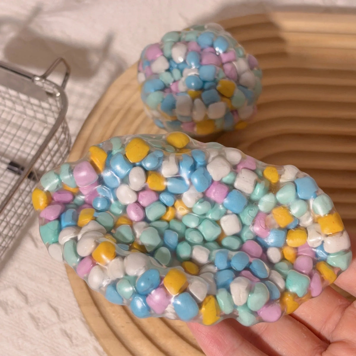 A colorful, squishy sensory stress ball with pastel blue, pink, yellow, and white confetti is held in a hand.