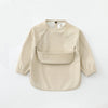 A beige waterproof long-sleeve art smock for toddlers with a rounded neckline and patch pockets.