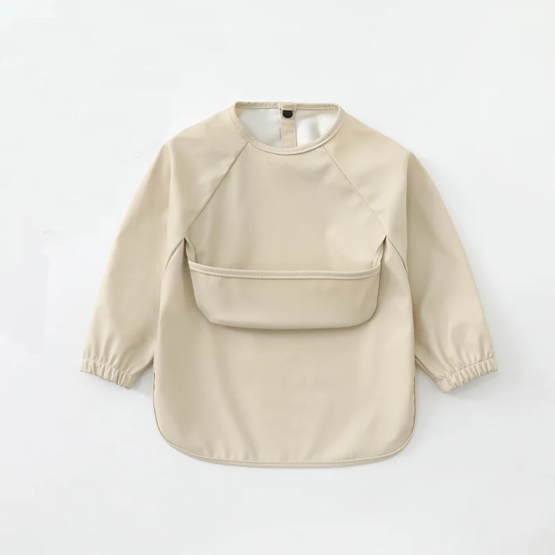 A beige waterproof long-sleeve art smock for toddlers with a rounded neckline and patch pockets.