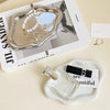 A clear glass perfume bottle rests on a white cloud-shaped tray next to a box featuring silver jewelry.