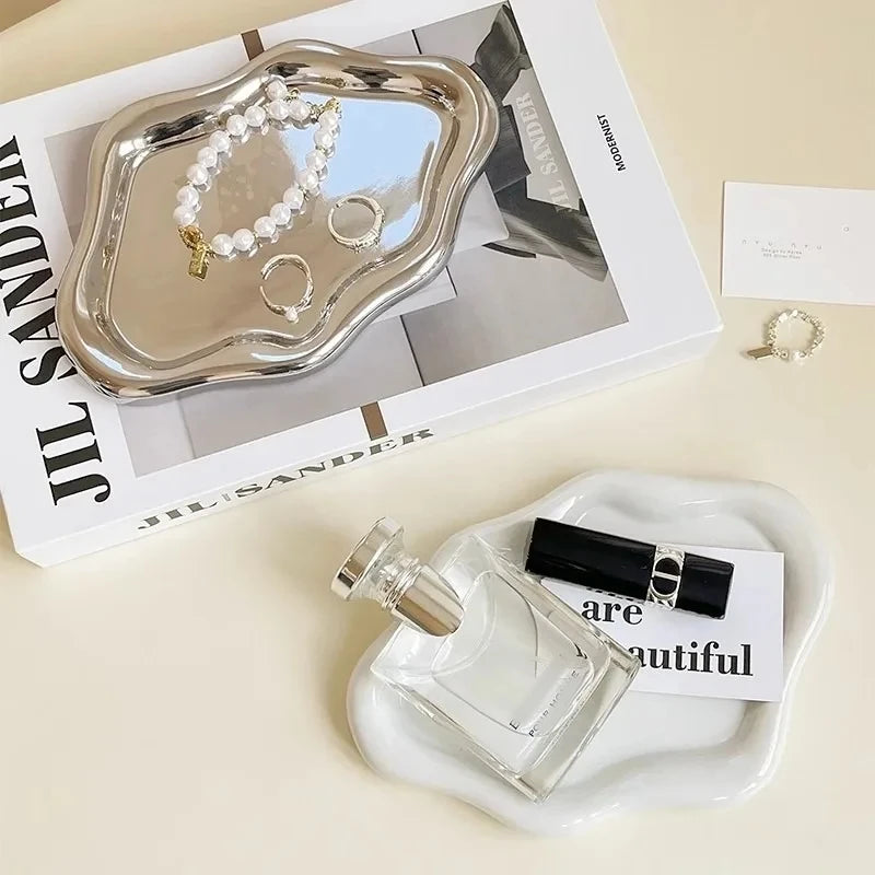 A clear glass perfume bottle rests on a white cloud-shaped tray next to a box featuring silver jewelry.