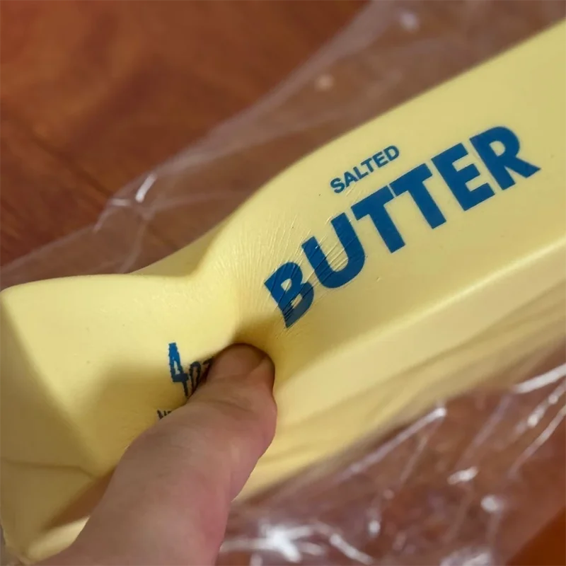 A hand is squeezing a yellow salted butter stick fidget toy with the word BUTTER visible on the stick.