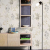 A wall features a light beige wallpaper with a pattern of green and white leaves, next to a wooden shelf unit and a modern wa