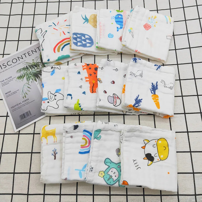 A collection of white cotton muslin baby washcloths featuring various colorful patterns and illustrations.