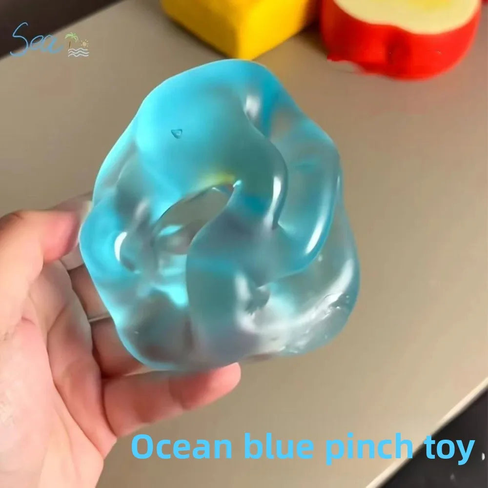 A hand holds a translucent ocean blue pinch toy stress ball against a light background.