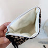 A hand holds open a leopard print cosmetic bag with a secure zipper, showing the light inner lining.