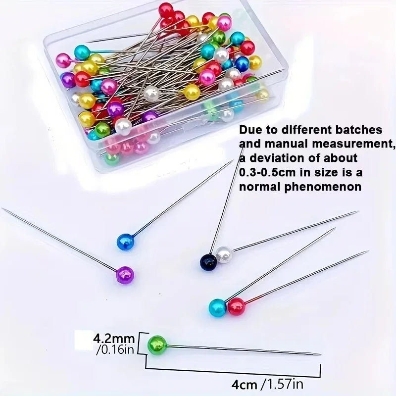 A clear container holds various pearlized ball head sewing pins of different colors and sizes.