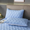 Light blue quilted pillow protector with envelope closure resting on a bed.