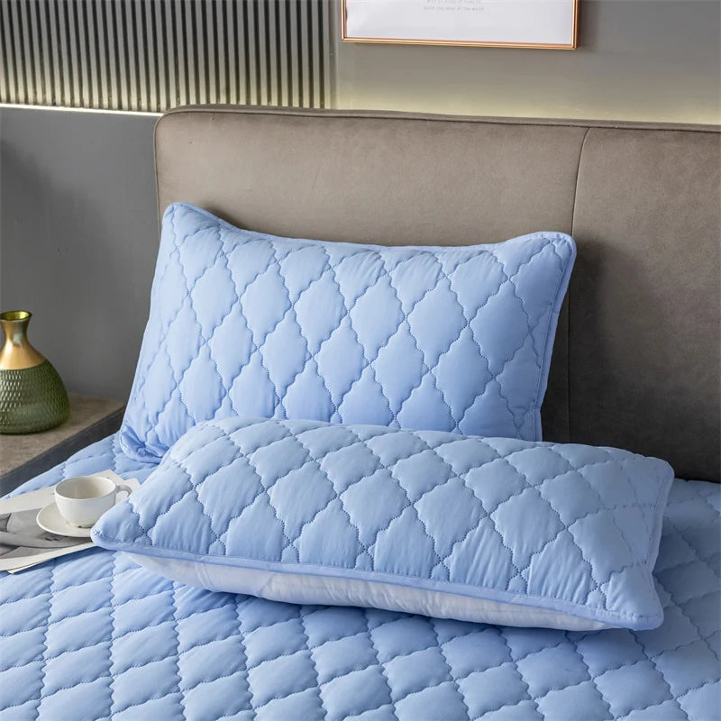Light blue quilted pillow protector with envelope closure resting on a bed.
