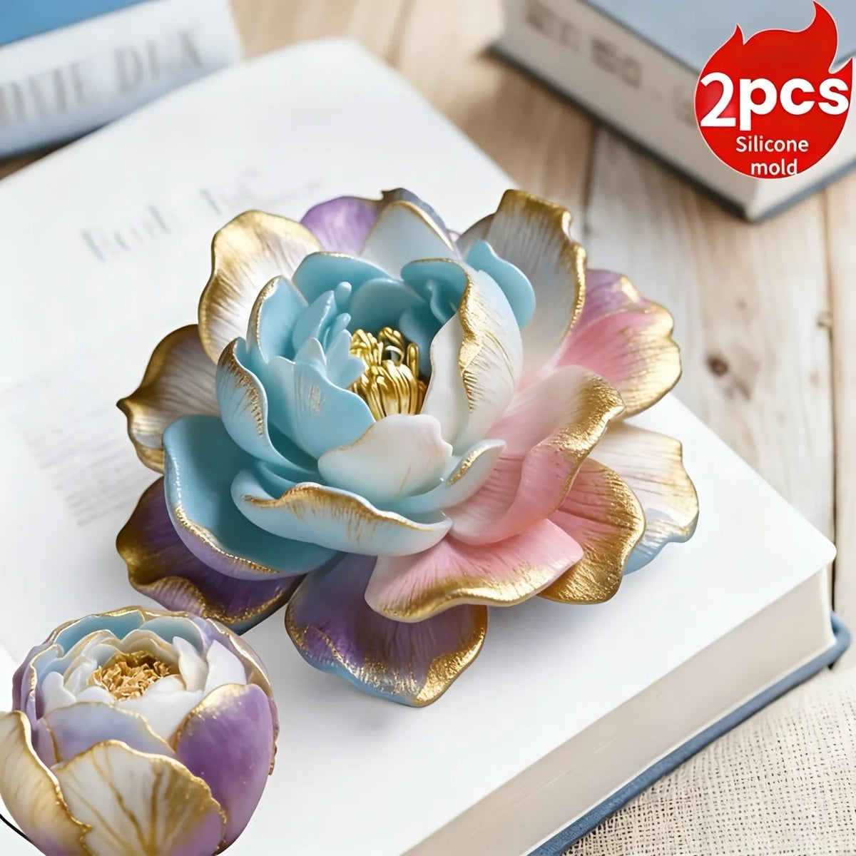 A light blue and pink 3D rose silicone mold with gold accents resting on a white book.