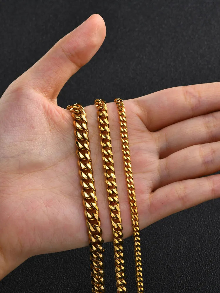 Three gold-colored stainless steel Cuban link chains displayed in a person's hand.
