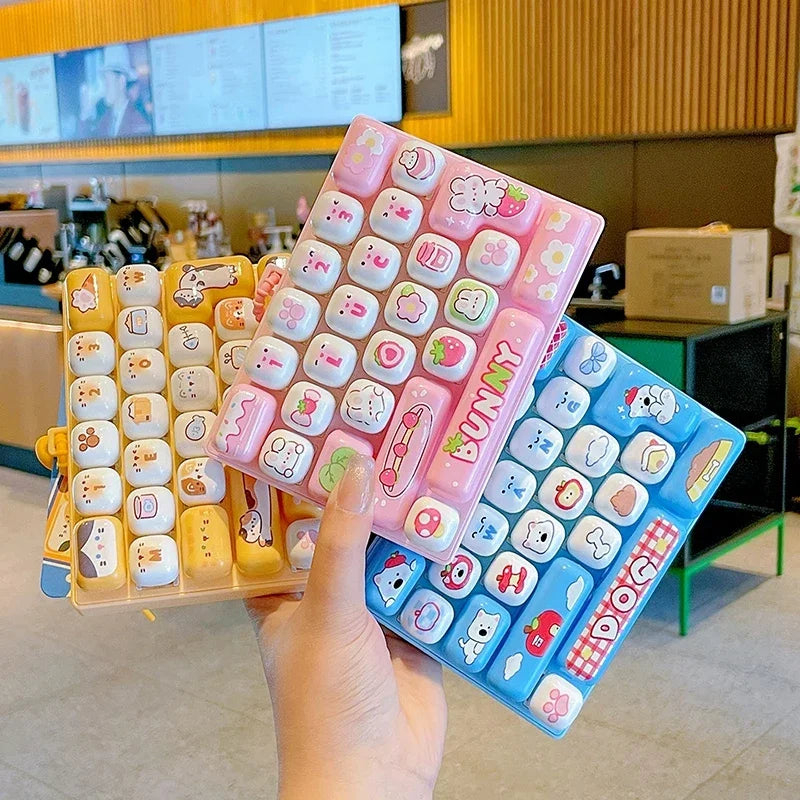 A hand holds a pink and blue cartoon keycap fidget keychain featuring various cute animal designs.