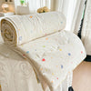 A cream-colored lightweight quilt with colorful scattered stars and hearts rolled up on a bed.