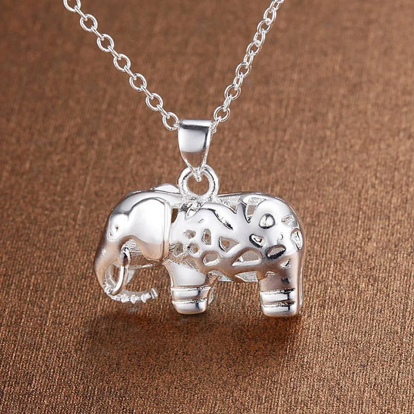 Un pendentif en argent sterling de forme d'éléphant sur une surface texturée marron.