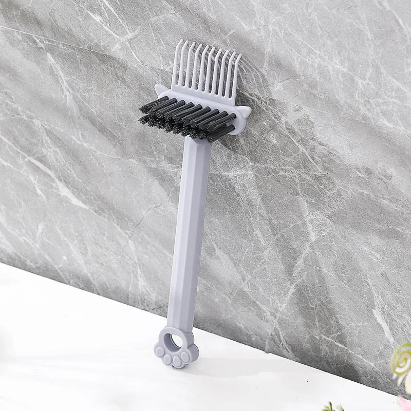 A gray dual-sided hairbrush cleaner with rake teeth is shown against a marbled background.