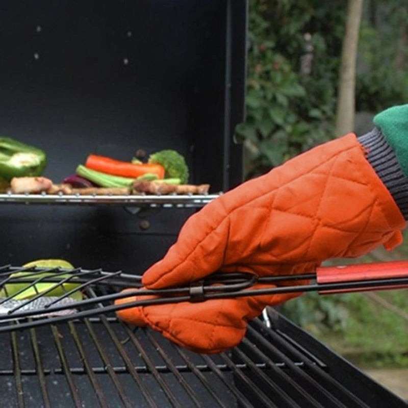 A hand wearing an orange quilted oven mitt is holding grilling vegetables over a black grill grate.