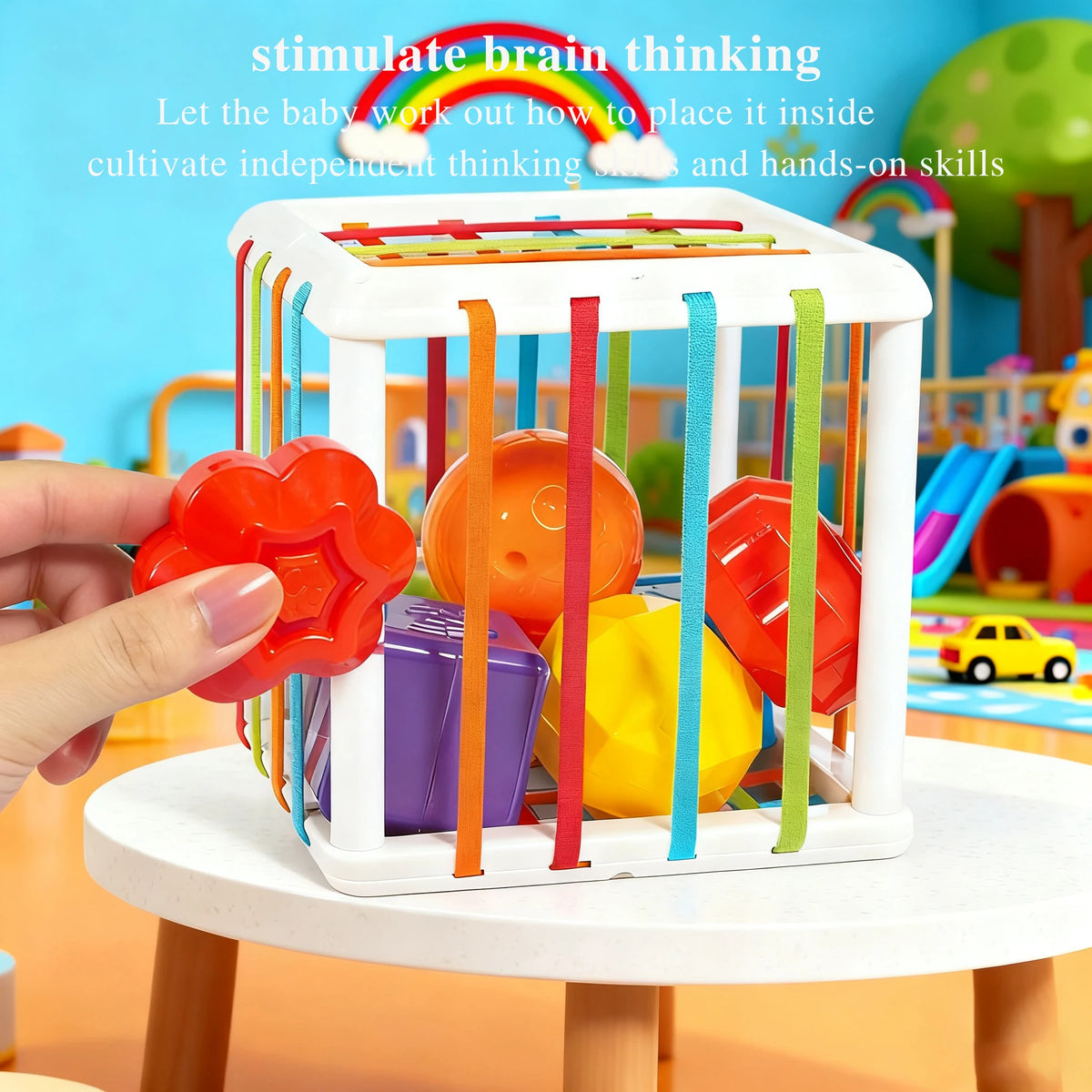 A hand places various colored plastic shapes and balls into a white Montessori sensory toy with colorful hanging strips.