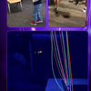 A bright pink glow-in-the-dark string launcher toy is shown with various colored strings and a green light effect.