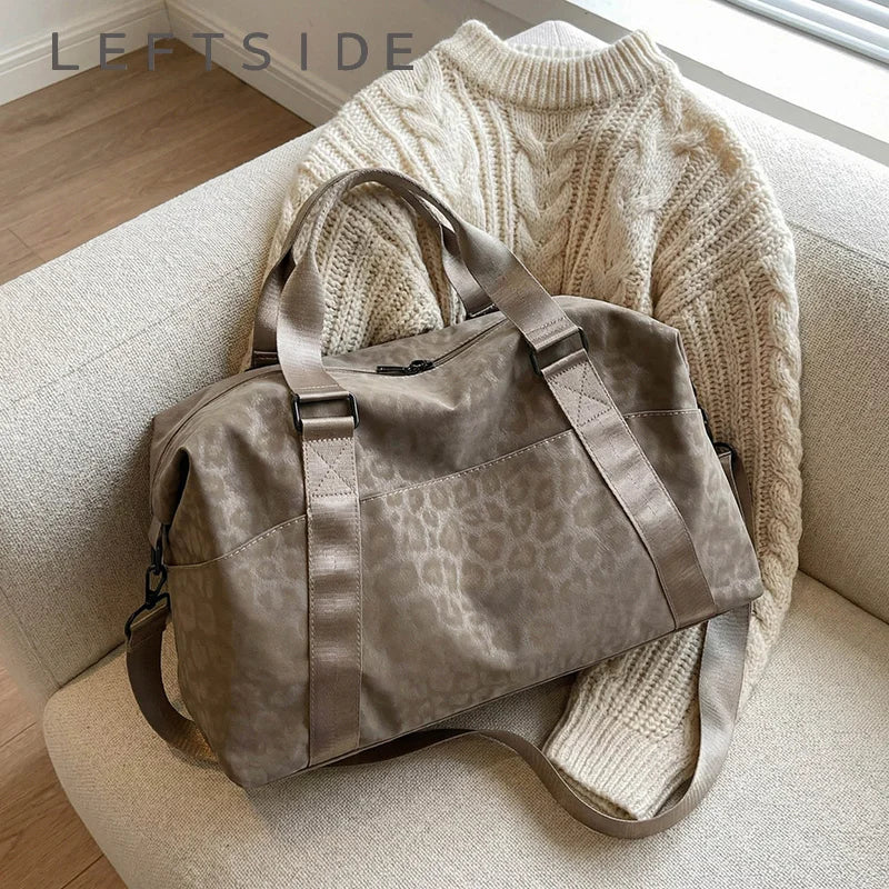 A taupe leopard print duffle bag resting on a light-colored sofa next to a cream knit sweater.