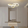 A modern pendant light fixture with a curved, glowing white design hangs above a minimalist counter in a light-colored room.