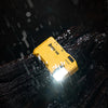 A yellow Wuben G5 compact rechargeable flashlight is illuminated, shining light onto a dark, wet surface.