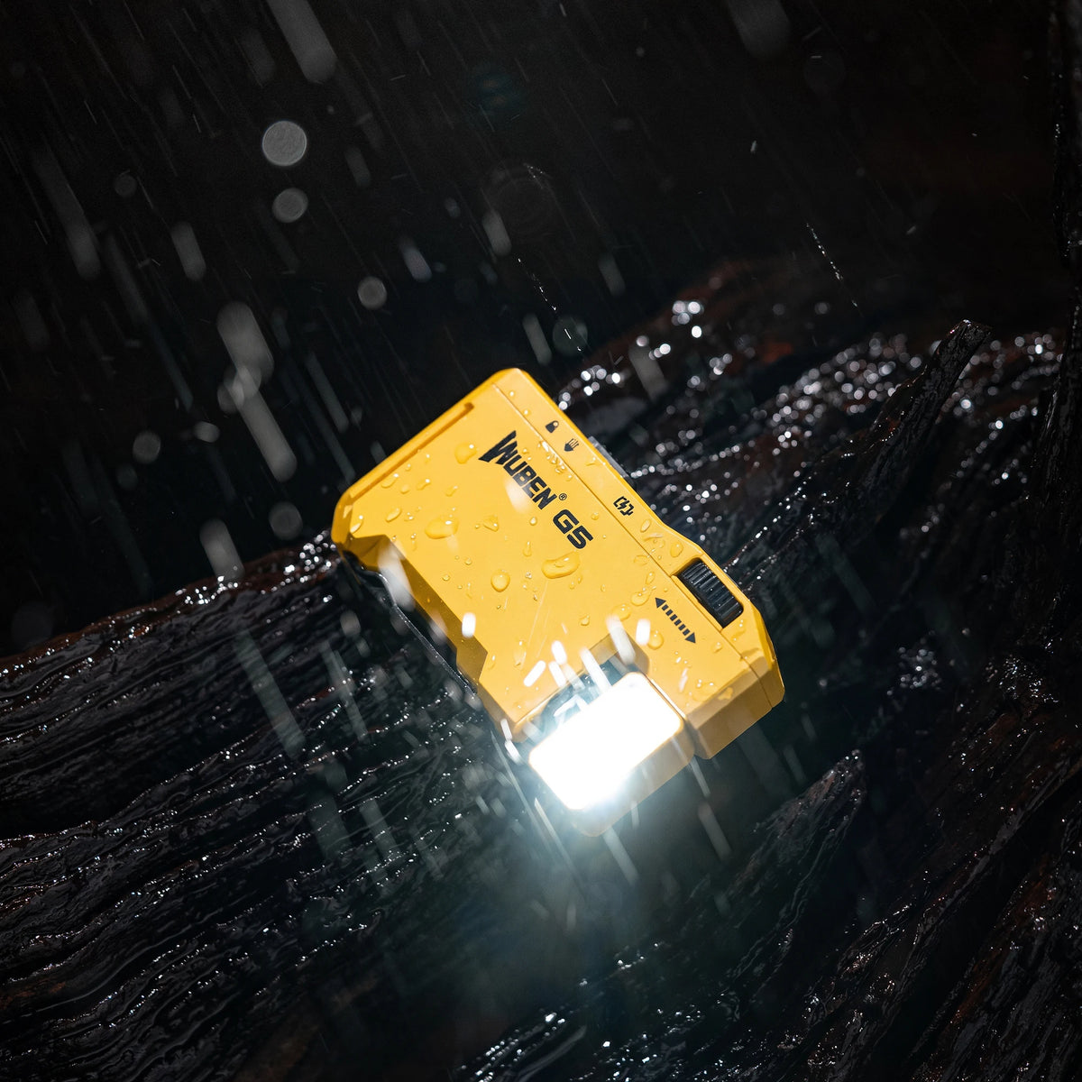 A yellow Wuben G5 compact rechargeable flashlight is illuminated, shining light onto a dark, wet surface.