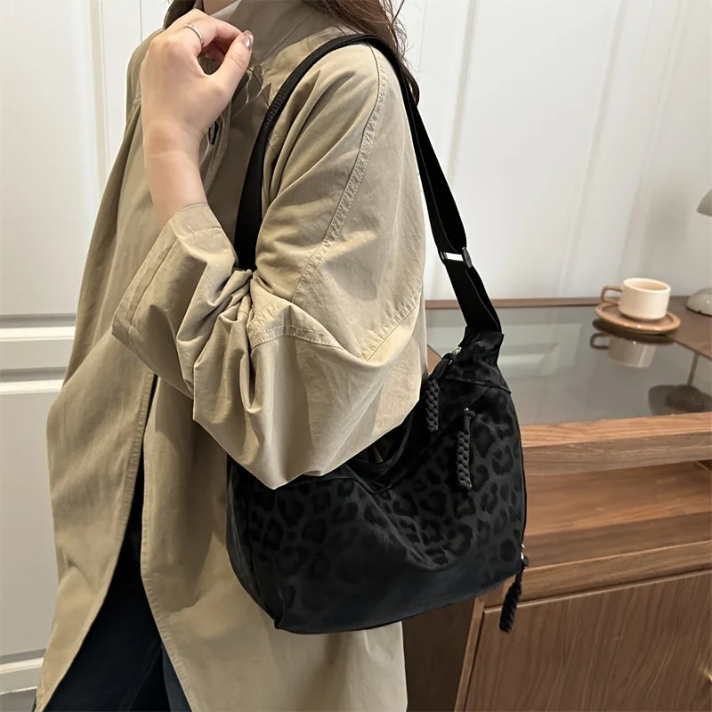 A woman wearing a beige shirt holds a black leopard print crossbody bag.