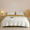 A white quilted duvet cover set with two pillows resting on a bed against a light wall.