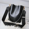 Black faux alligator pattern crossbody bag with black strap resting on white fur