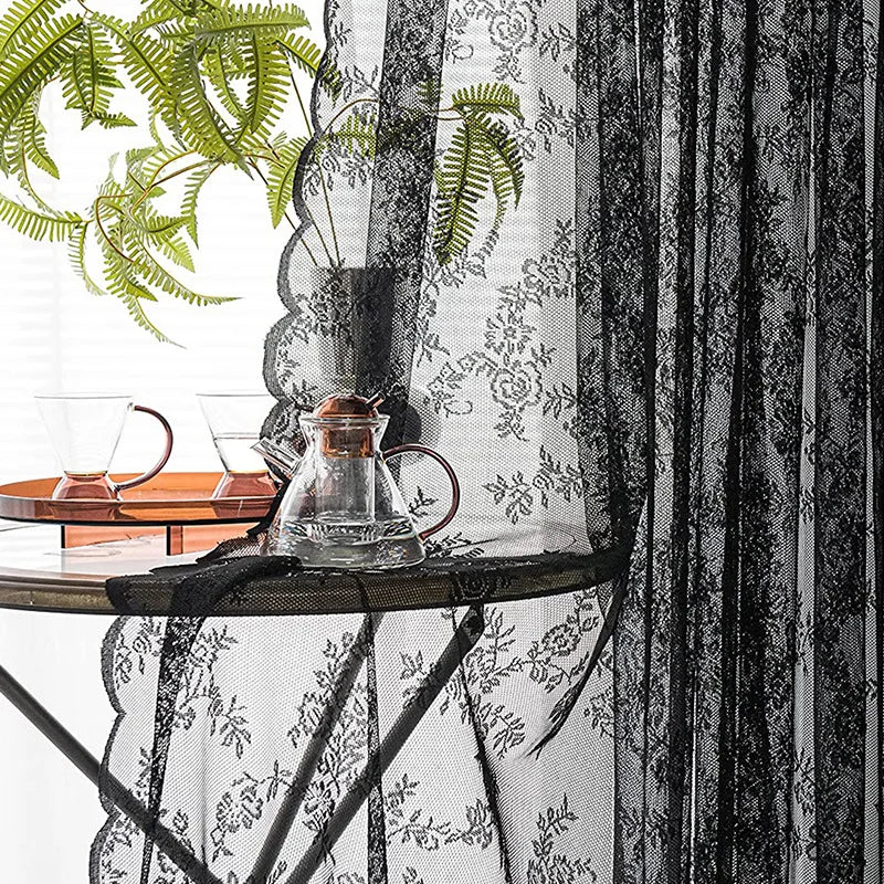 Rideaux en dentelle florale noire drapés à côté d'une théière et de tasses à thé sur une table.