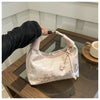 Hellrosa Seiden-Crossbodybag mit Perlenstickerei wird von einer Hand auf einer Holzoberfläche gehalten.
