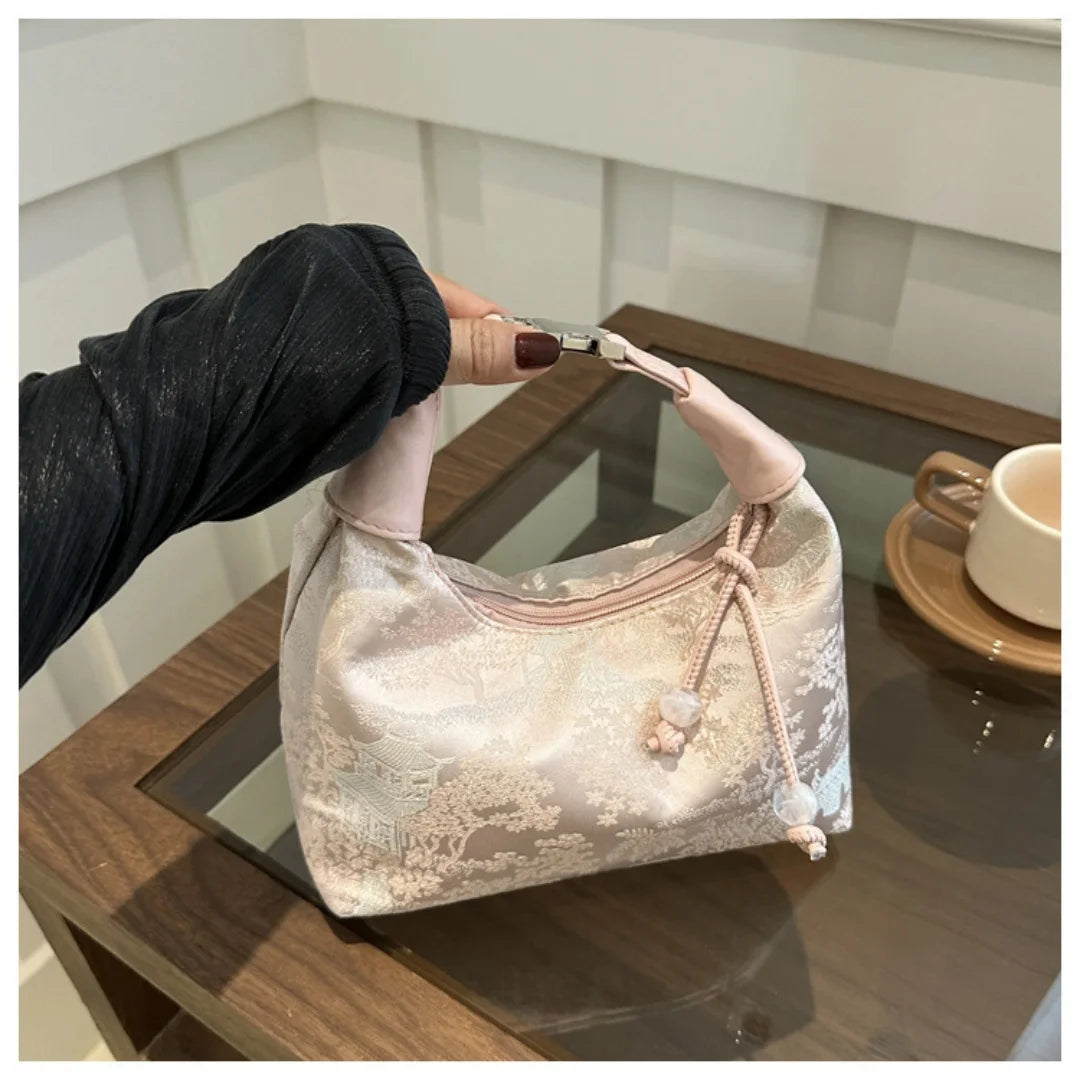 Hellrosa Seiden-Crossbodybag mit Perlenstickerei wird von einer Hand auf einer Holzoberfläche gehalten.