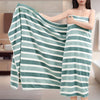 A woman holds an oversized striped microfiber bath towel in a teal and white stripe pattern.