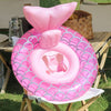 Pink inflatable swim ring with a scale pattern resting on a wooden table.