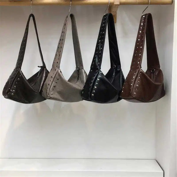 Eine Reihe von vier Punk-Nieten-Design-Schultertaschen in schwarzem, grauem und braunem Leder, die an einem Holzständer hänge